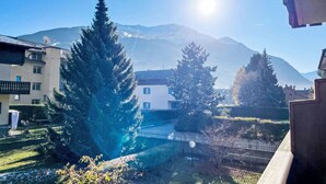 A residential area with a mountain in the background, a white building with blue windows, and a large evergreen tree in the foreground. - Monte Confinale Garden View by Interhome (Bormio)