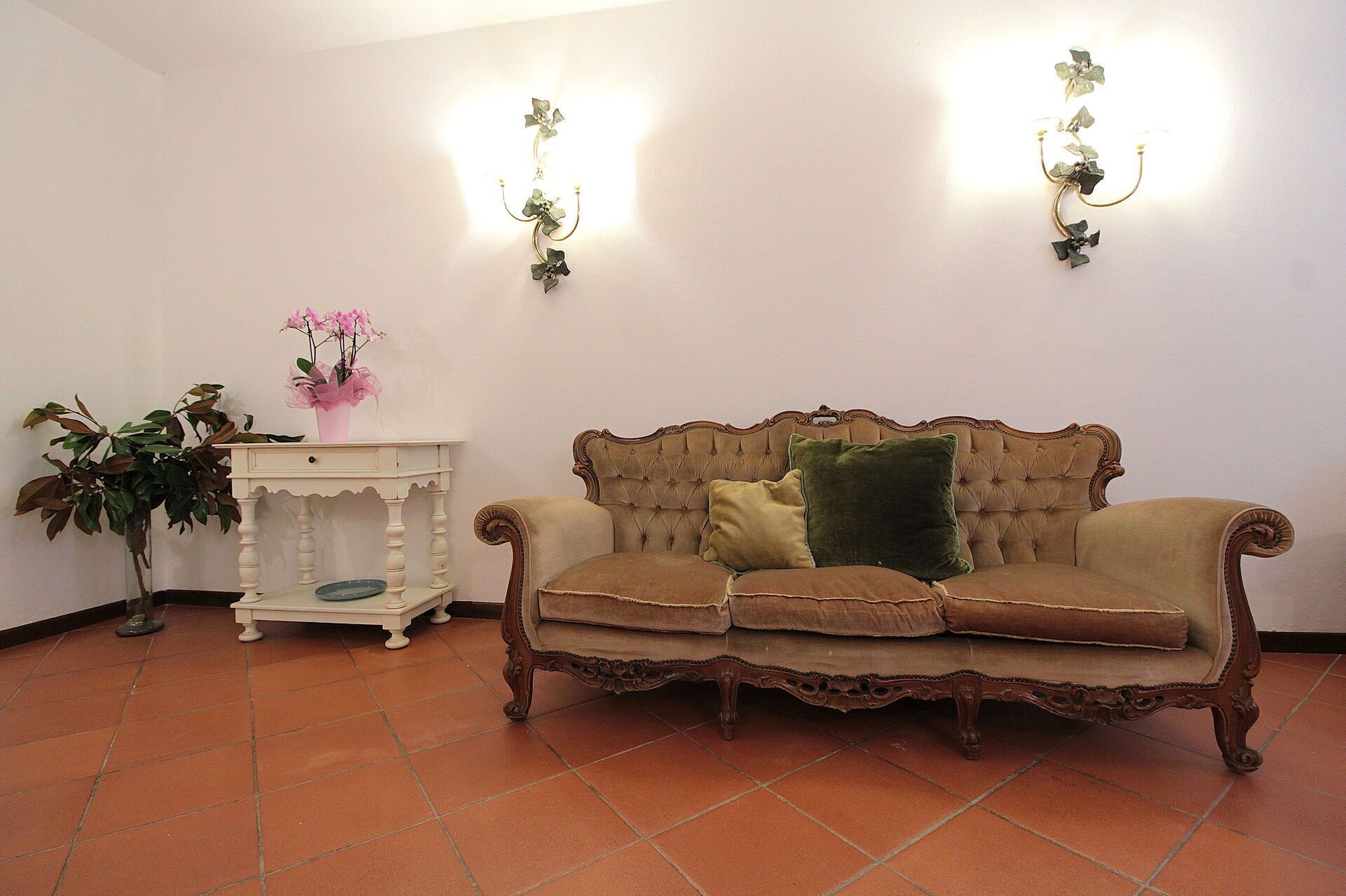 Una habitación con un sofá de estilo vintage, una mesita auxiliar blanca con un florero y dos apliques de pared.