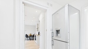 A modern kitchen with a white refrigerator, wooden flooring, and a dining area with a table and chairs.