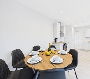 Un comedor moderno con una mesa redonda dispuesta para seis personas, sillas tapizadas negras y una cocina al fondo.