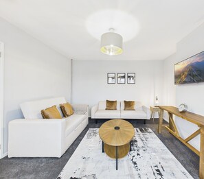 Una sala de estar moderna con un sofá blanco, una mesa de centro redonda y una mesita de noche de madera.