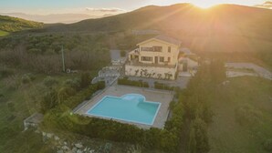 Une maison à deux étages avec une piscine, entourée de collines et sous un ciel dégagé.