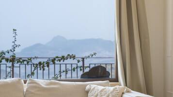 A room with a beige sofa, a wooden side table, and a view of mountains through a window with a curtain.