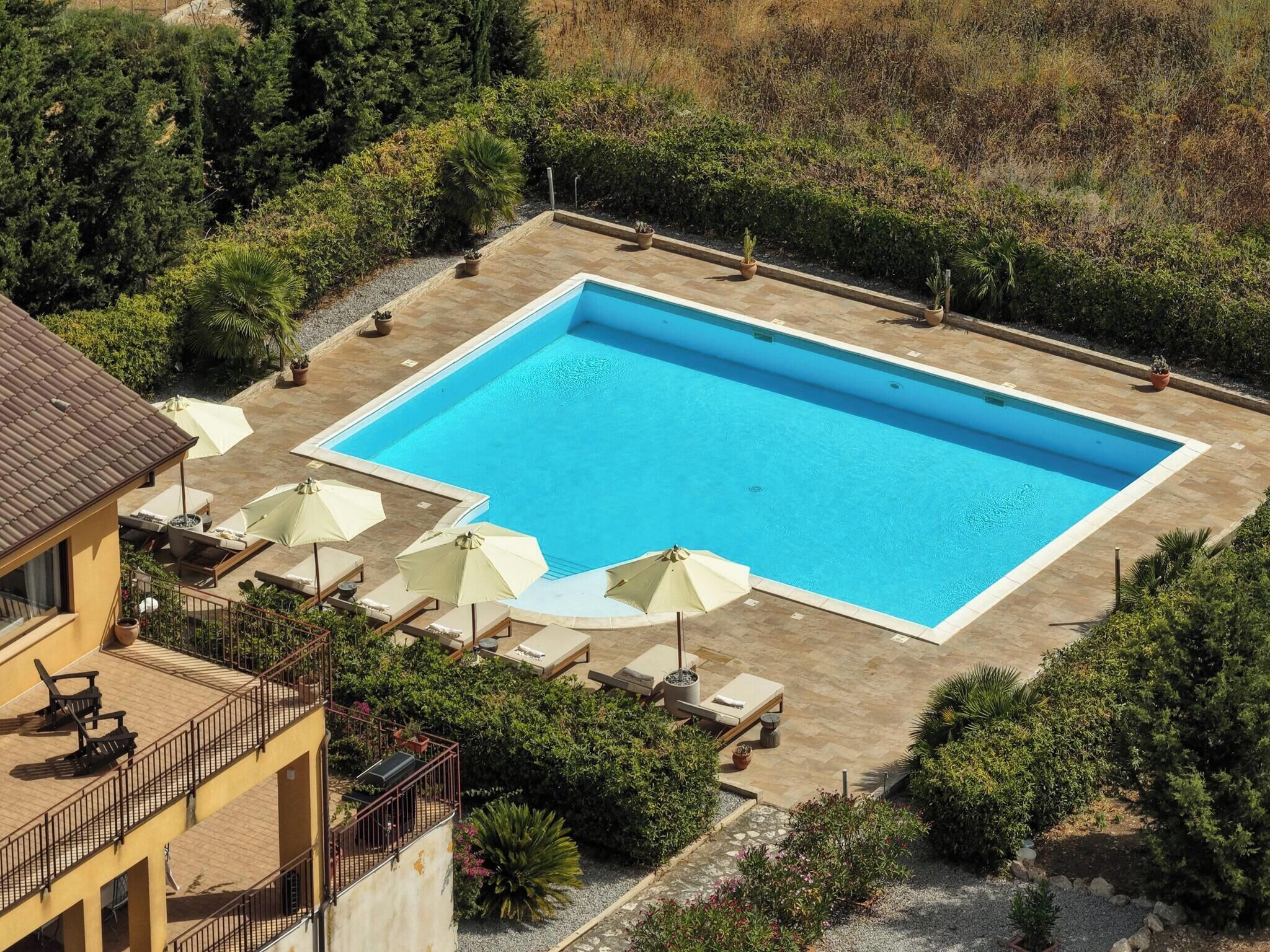 A rectangular swimming pool with a tiled deck surrounding it, equipped with several lounge chairs and umbrellas.