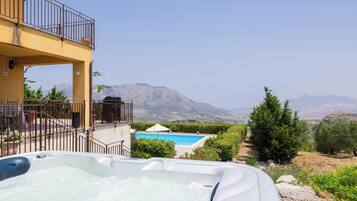Un jacuzzi con vista a la montaña, una piscina y un balcón con barandilla.