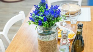 A wooden dining table with a vase of blue flowers, a bottle, a basket of eggs, and two empty wine glasses. - VILLA GINEVRA: typical Salento pajara with swimming pool in the Salento countryside. (Montesano Salentino)