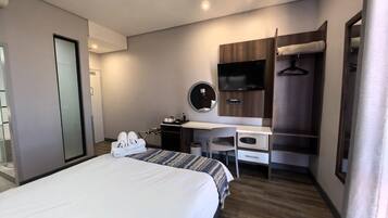 A hotel room with a bed, a desk, a mirror, a TV, and a wardrobe.