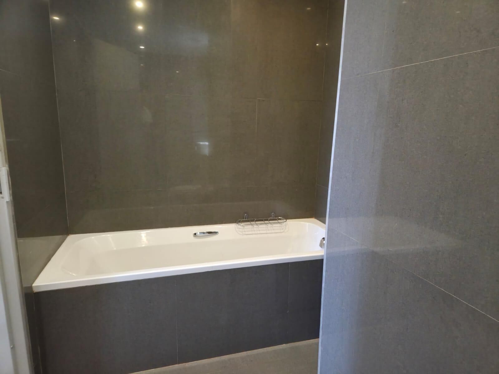 A modern bathroom with a freestanding bathtub, dark tiled walls, and a visible shower area.