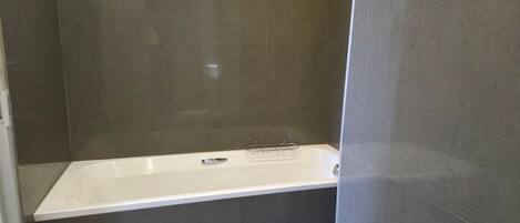 Une salle de bain moderne avec une baignoire sur pieds, des murs recouverts de carreaux foncés et un espace douche bien délimité.
