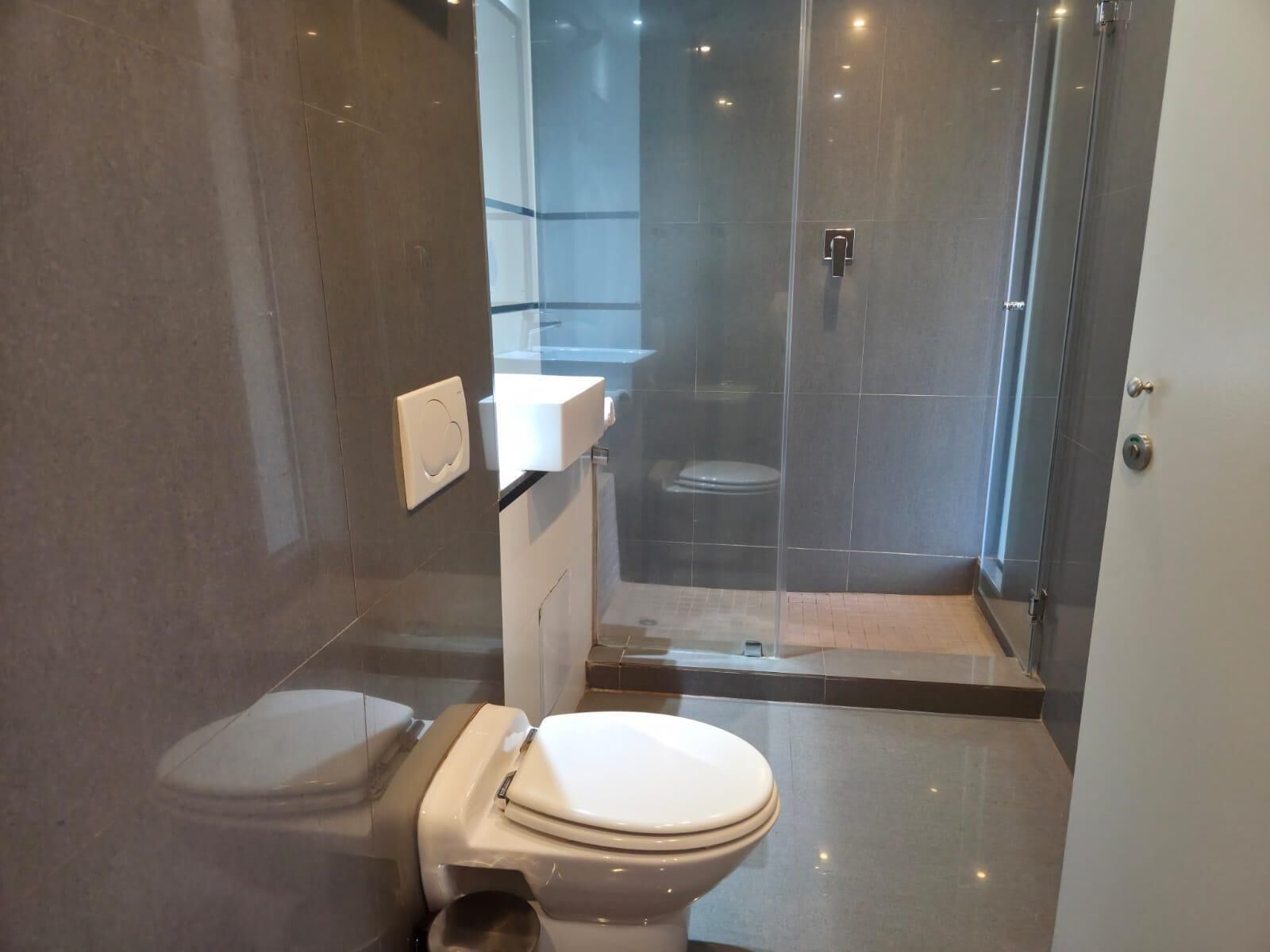 Een moderne badkamer met toilet, douchecabine en glazen wand.