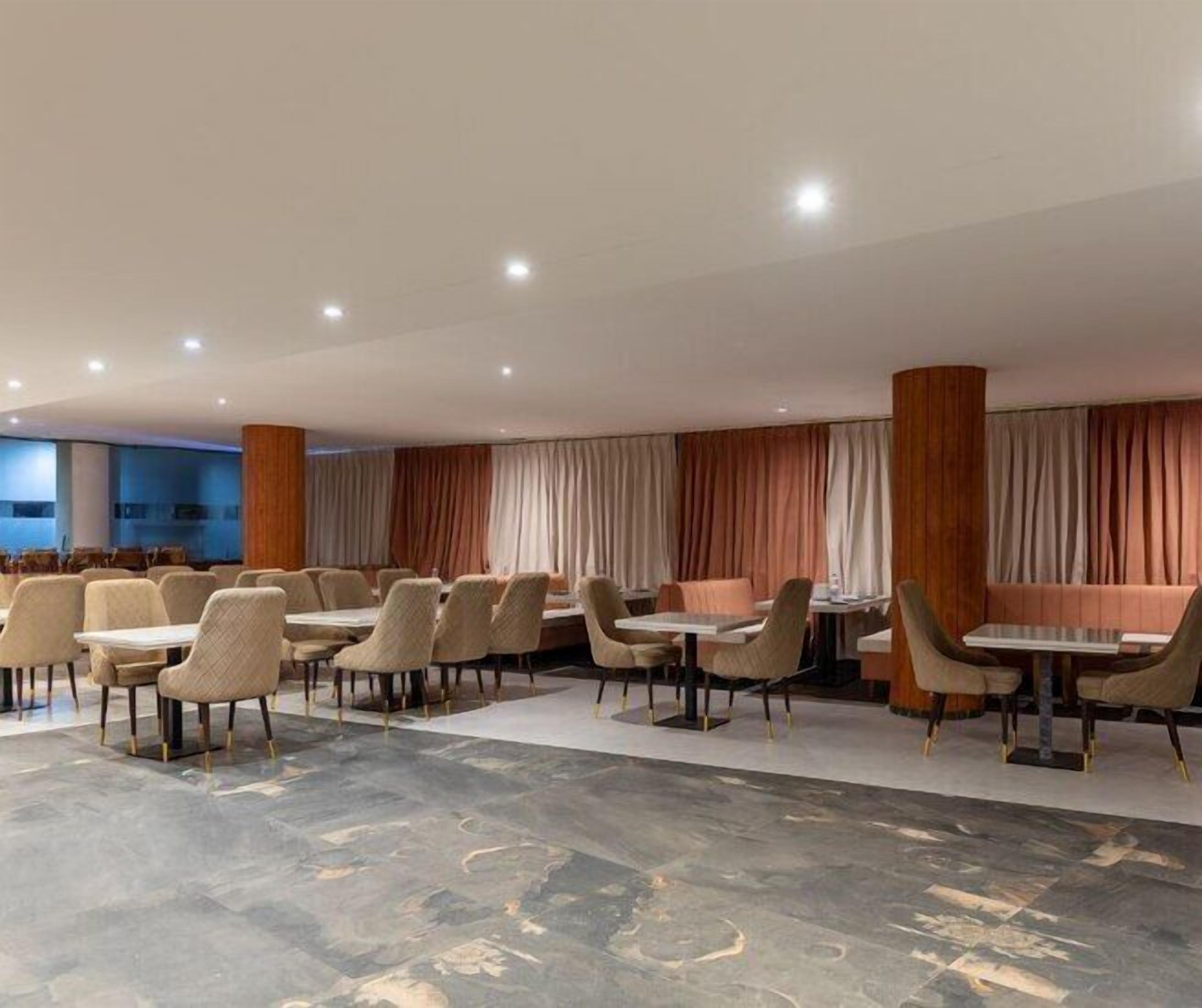 A modern dining area with multiple tables and chairs, a patterned floor, and a large window with curtains.