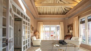 A spacious living room with a high ceiling, a large window with curtains, a sofa, a small table, and a door leading to another room. - Villa Castro (Granada)
