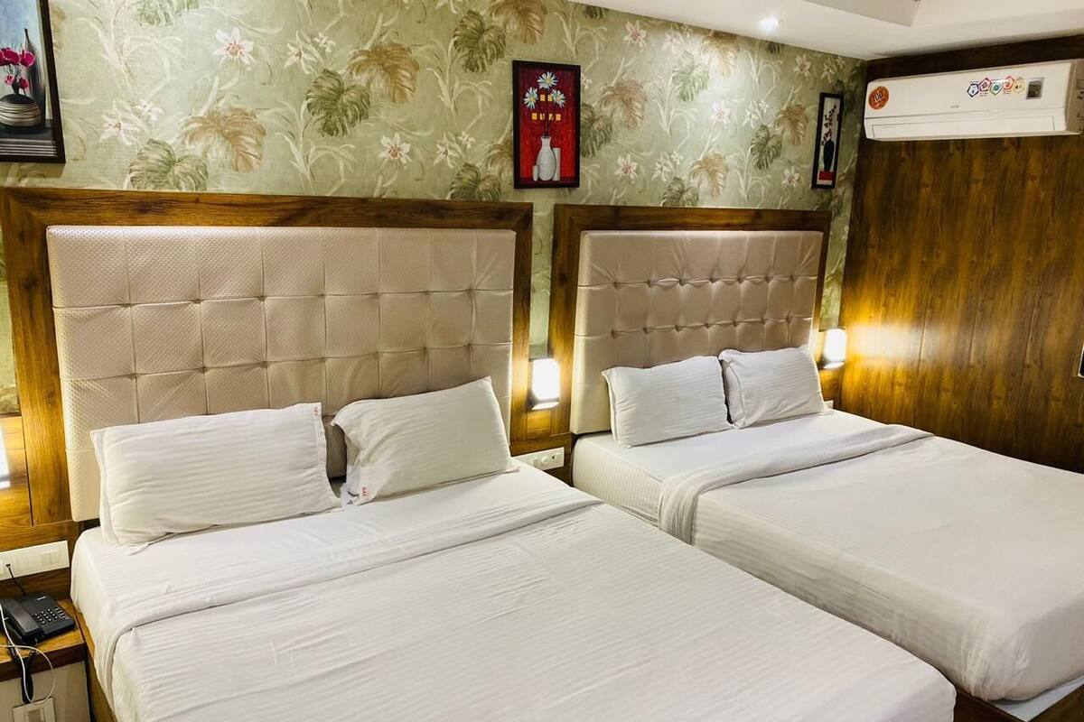 A hotel room with two beds, wooden headboards, and a floral wallpaper design.