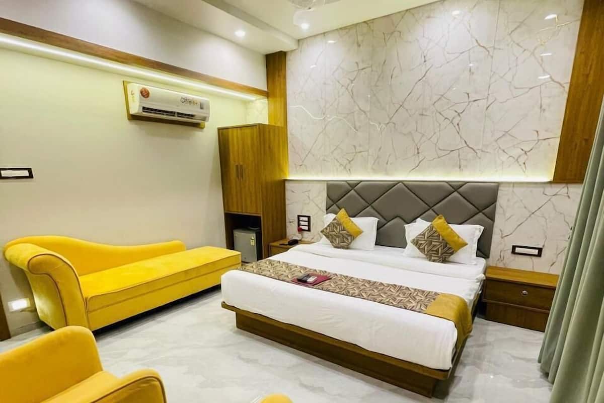A modern hotel room with a large bed, a yellow sofa, a small table, and a ceiling fan.