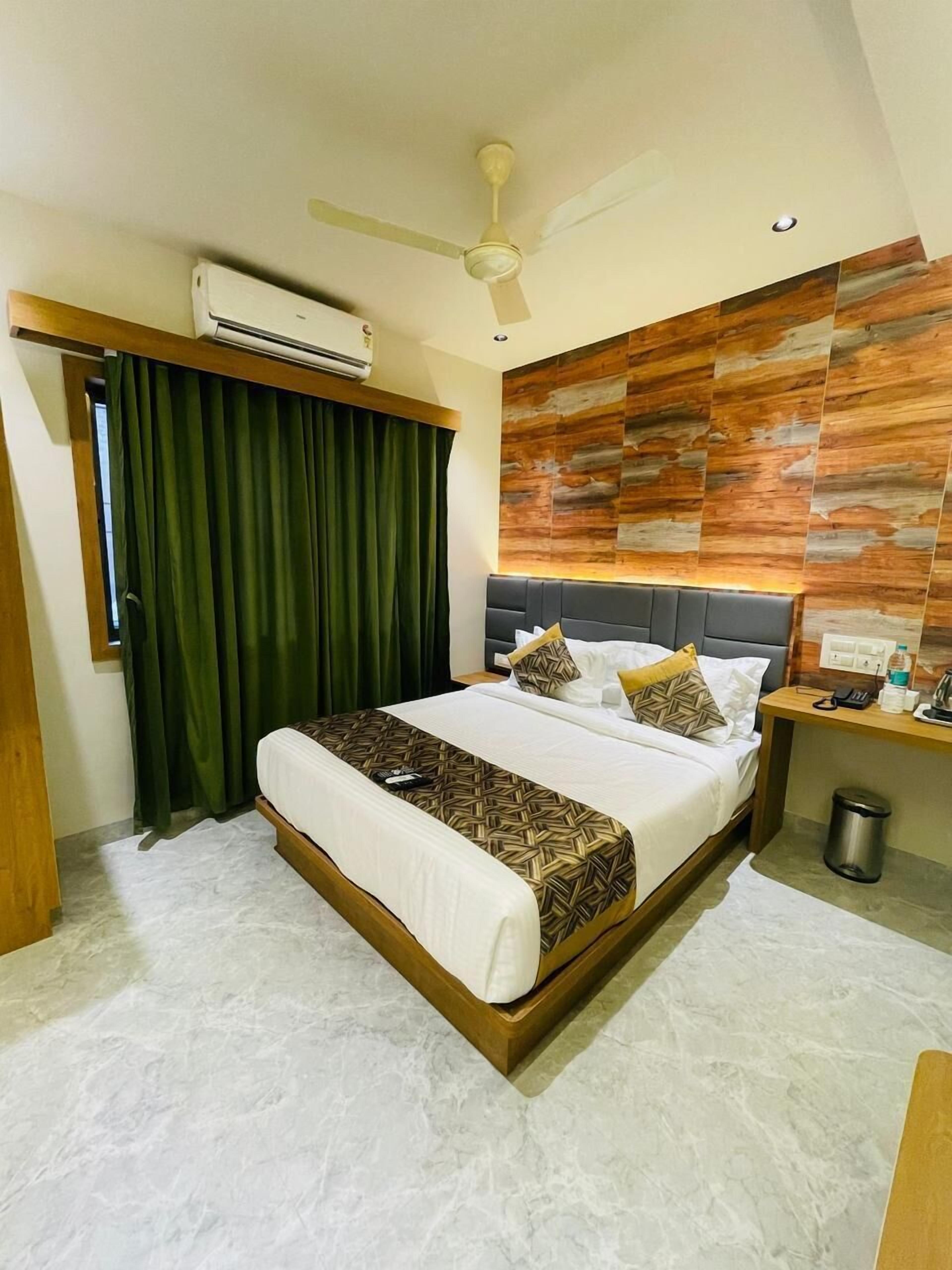 A hotel room with a large bed, a ceiling fan, an air conditioning unit, a wooden headboard, and a wall with a wood-like pattern.