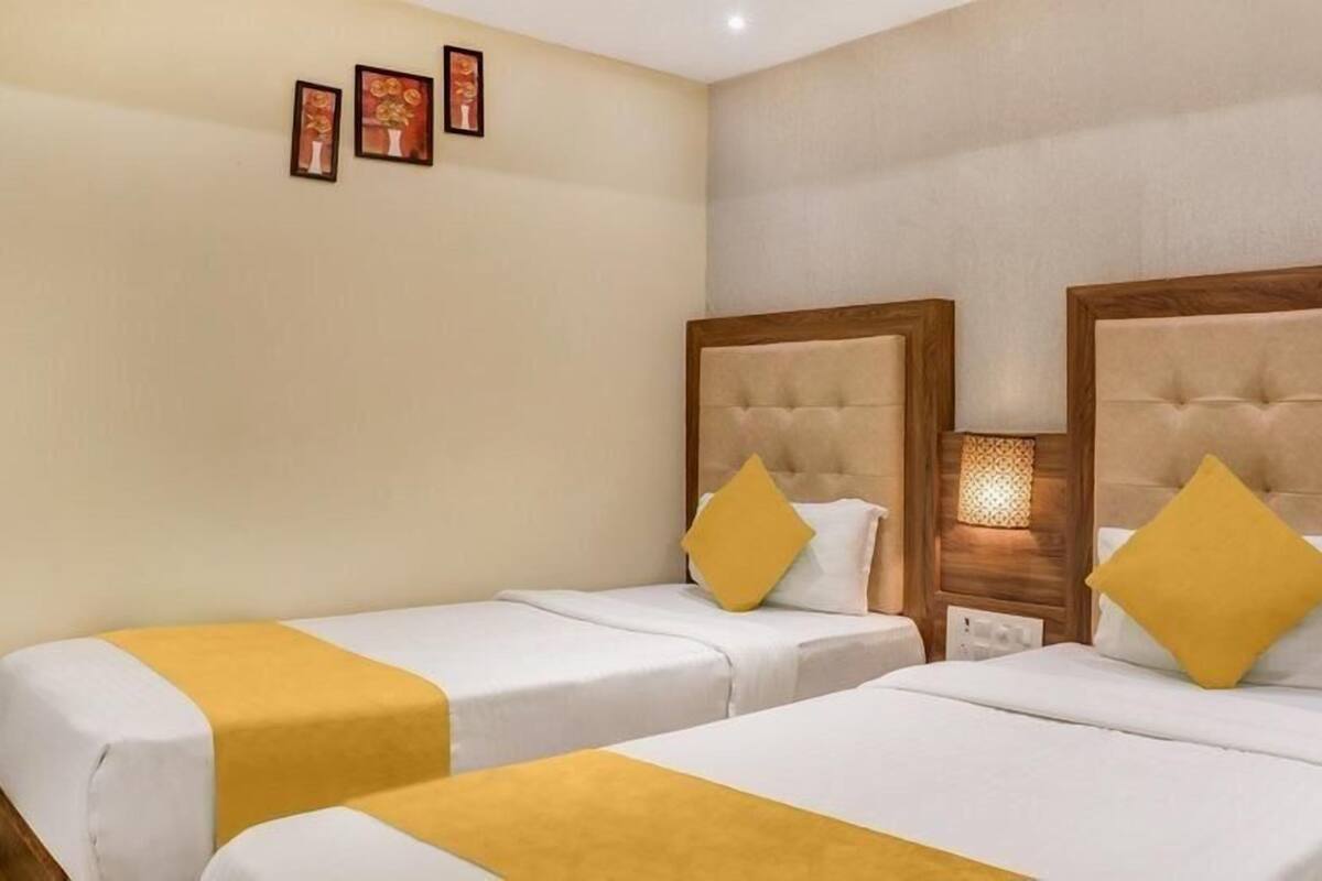 A hotel room with two beds, each with a wooden headboard and a yellow accent pillow.