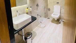 Ein modernes Badezimmer mit Marmorwand, schwarzem Waschtisch, weißem Waschbecken, Toilette und Duschbereich.