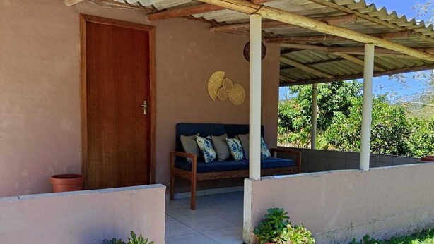 Eine überdachte Veranda mit einer Holztür, einem blauen Sofa mit Kissen und zwei Blumentöpfen.