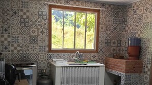 Eine Küche mit gemusterten Fliesen, einem Fenster mit Blick auf Grünflächen, einem Spülbecken und einem Backofen aus Ziegelsteinen.