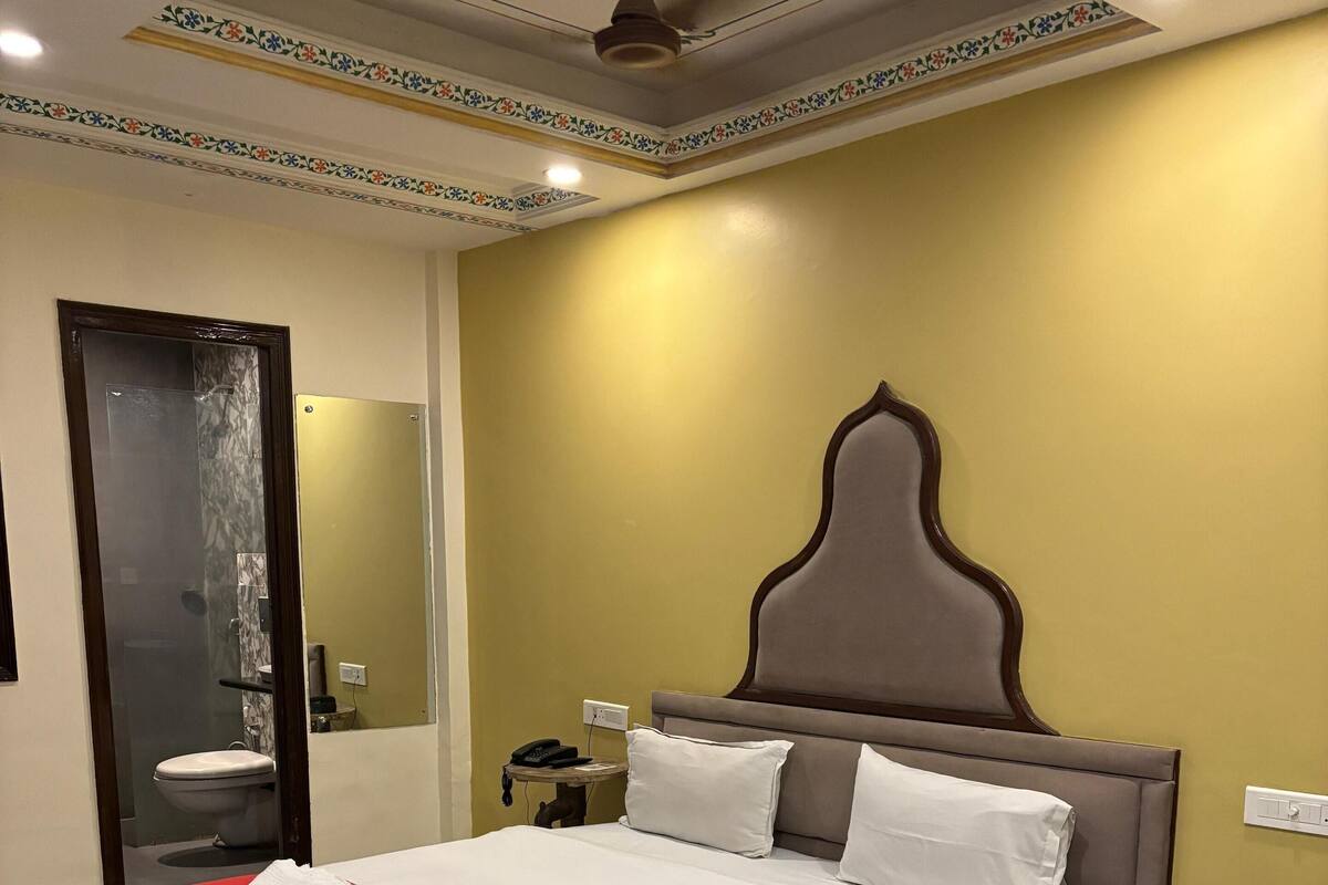 A hotel room with a large bed, a bedside table with a phone, a mirror, and a ceiling fan.