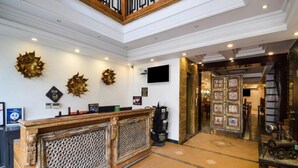 A reception area with a wooden counter, decorative wall art, and a tiled floor. - The Umed (Jodhpur)
