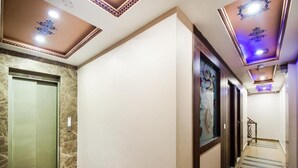 A hotel hallway with a marble elevator, a staircase, and a wall with a framed artwork. - The Umed (Jodhpur)