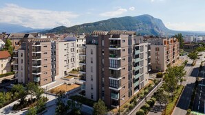 Ein modernes Apartmenthaus mit mehreren Etagen, Balkonen und Blick auf einen Berg im Hintergrund.