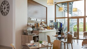 Ein modernes Café mit einer Frühstückstheke, Sitzgelegenheiten und großen Fenstern mit Blick ins Freie.