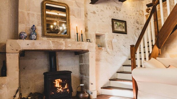 A stone fireplace with a wood-burning stove, a mirror above it, and a staircase leading to a second floor. - Le Clos du Maraicher Villandry (Villandry)