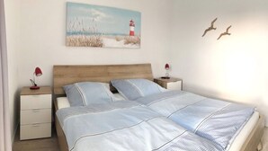 A bedroom with a wooden headboard, a bed with striped bedding, two bedside tables with lamps, a nightstand, and a painting of a lighthouse. - Great penthouse with 20 sqm roof terrace, North Sea view, sauna and hot tub! (Wangerland)