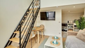 A modern living space with a staircase, a dining area with a table and chairs, a sofa, and a TV mounted on the wall. - Chic Duplex with AC • Bastille & Marais (Paris)