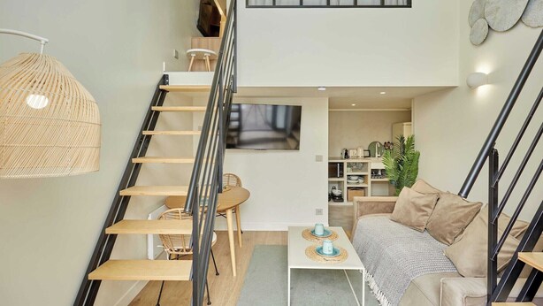 A modern interior with a staircase, a sofa, a dining table, and a hanging light fixture. - Chic Duplex with AC • Bastille & Marais (Paris)