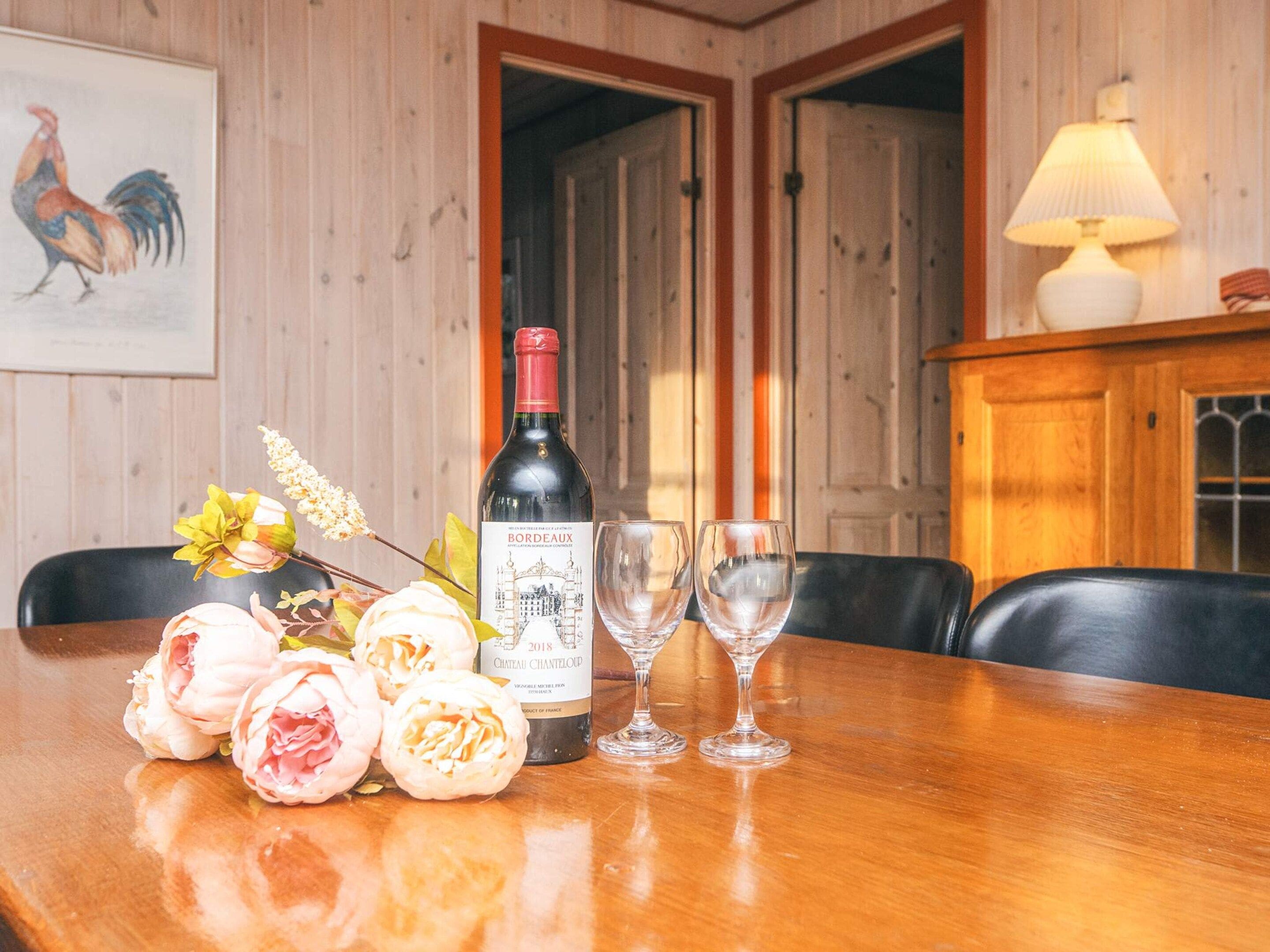 A wooden dining table with a bottle of wine, two glasses, and a bouquet of flowers.