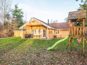 A wooden house with a covered patio, a green slide, and a wooden play structure.
