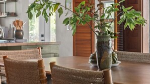 Et spiseområde med et træbord og fletstole, en vase med en plante og en loftlampe.