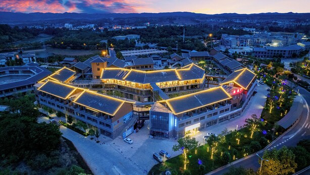 A modern building with multiple levels and a central courtyard, surrounded by greenery and a road. - Yi Jia Hotel (Kunming)