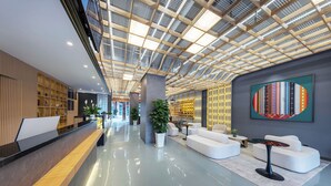 A modern lobby with a high ceiling, a reception desk, seating area, and a large artwork on the wall. - Yi Jia Hotel (Kunming)