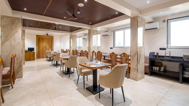 A modern dining area with marble flooring, wooden ceiling panels, and a mix of wooden and upholstered chairs. - Palette Hotel Pune, Midc Chinchwad (Pune)