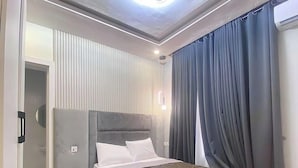 A modern bedroom with a bed, bedside tables, a ceiling light, and a view of the outside through a window with curtains.