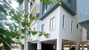 A multi-story residential building with a paved courtyard and a covered parking area.