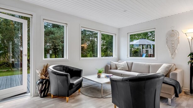 A modern living room with a sofa, two armchairs, a coffee table, and large windows offering a view of the outdoors.