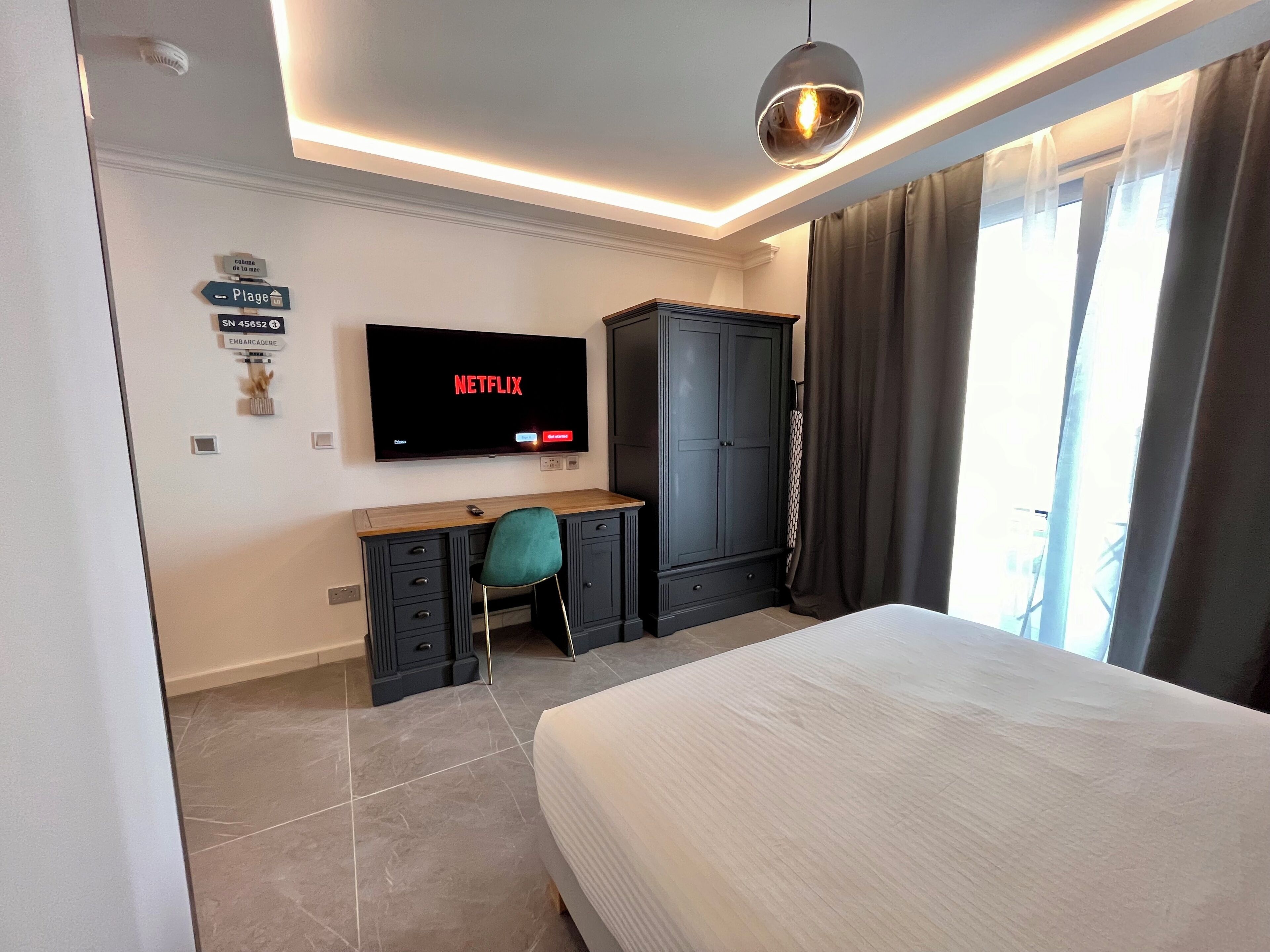 A hotel room with a bed, a desk with a chair, a TV mounted on the wall, and a wardrobe.