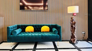A teal sofa with yellow cushions in a room with vertical wooden paneling and a modern ceiling design. - Sliema Studios (Sliema)