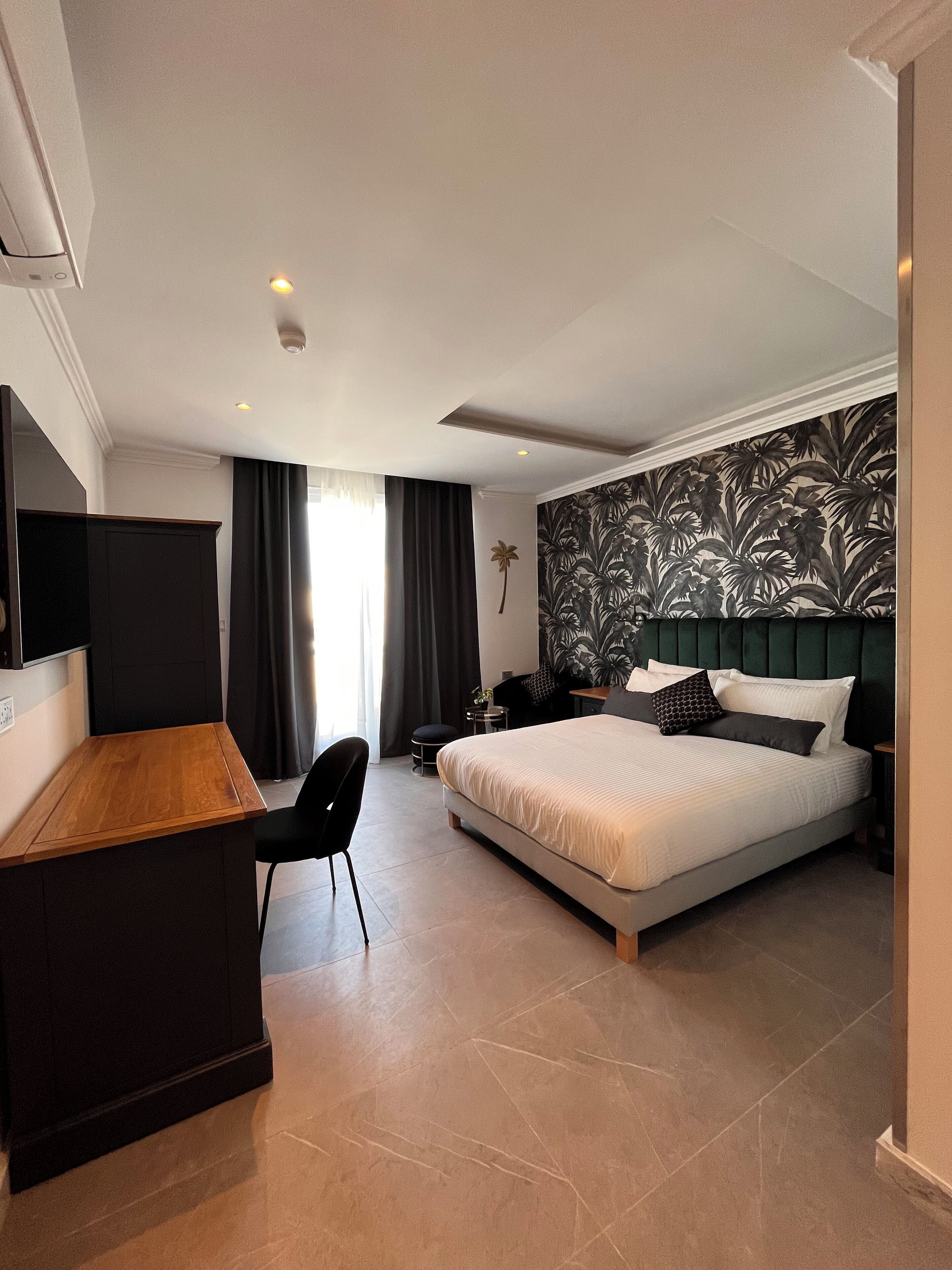 Ein Hotelzimmer mit Bett, Schreibtisch, Sessel, Nachttisch und einem an der Wand befestigten Fernseher.