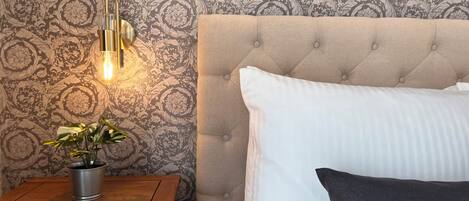 A bedroom with a tufted headboard, a bedside table with a plant, and a patterned wallpaper.