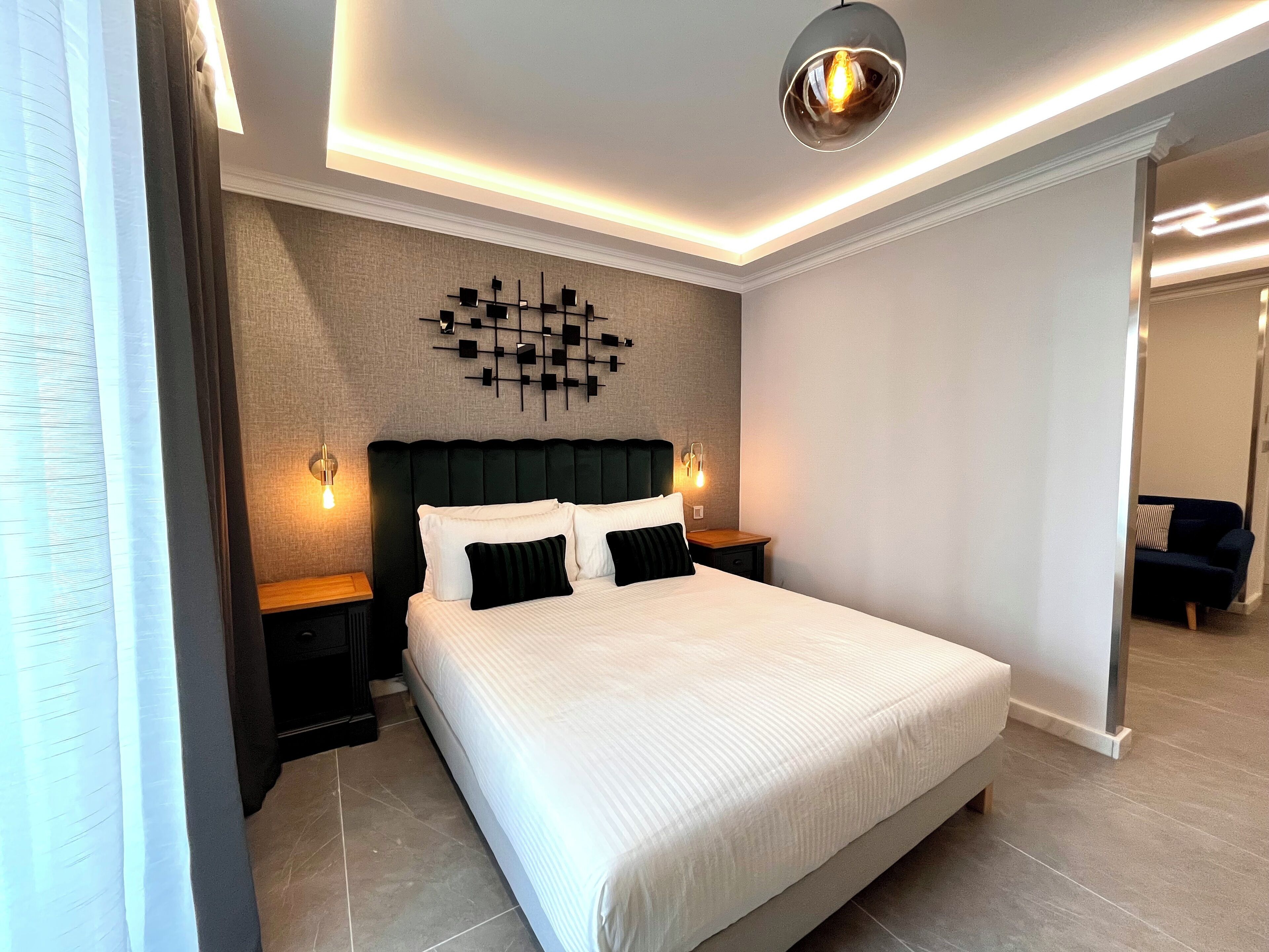 Un dormitorio moderno con una cama grande, dos mesitas de noche, una lámpara de pared y una obra de arte geométrica en la pared.