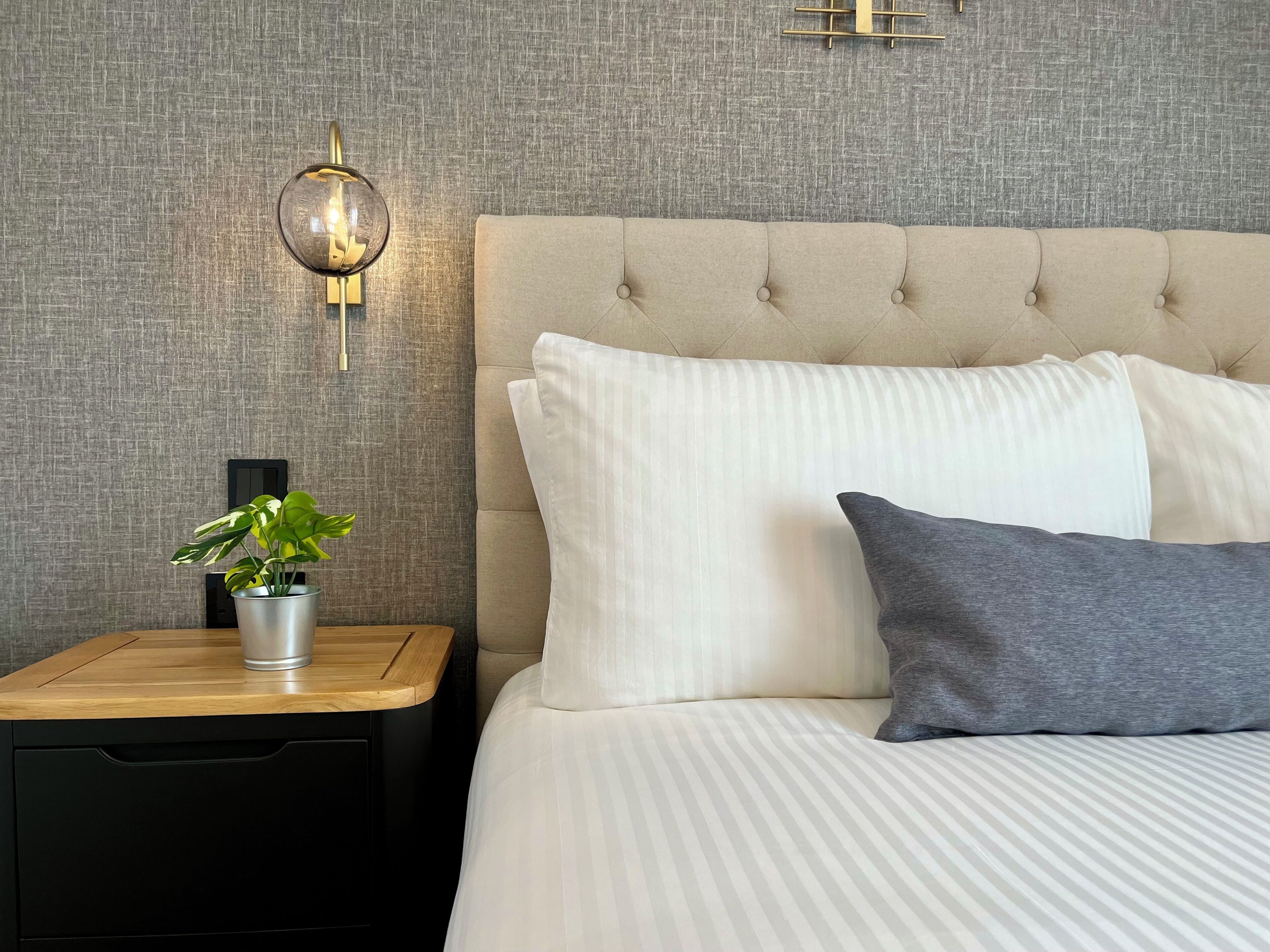 A neatly made bed with striped bedding, a tufted headboard, and a bedside table with a plant.