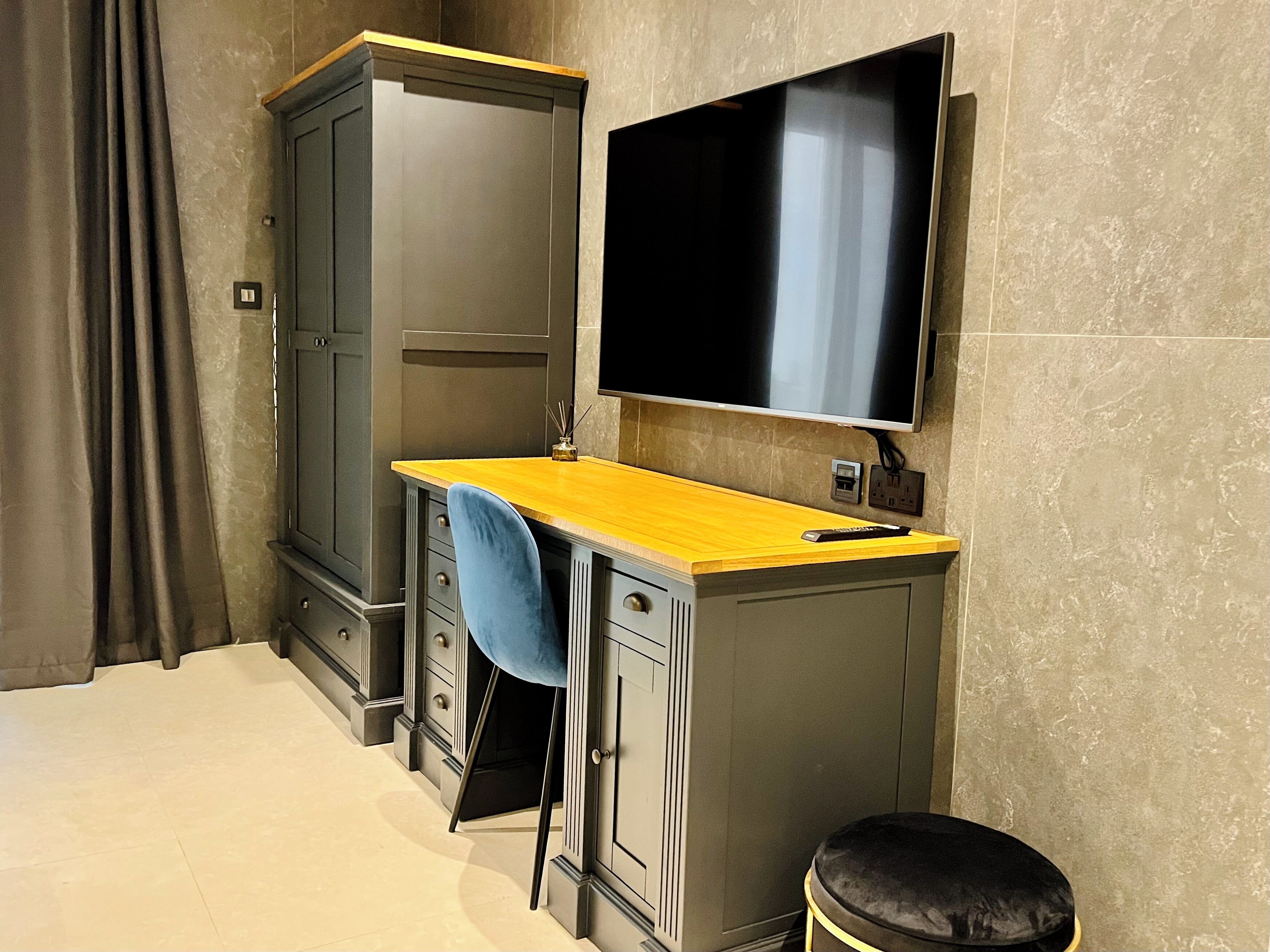Een kleine kamer met een bureau, een aan de muur bevestigde televisie, een kledingkast en een gordijn.