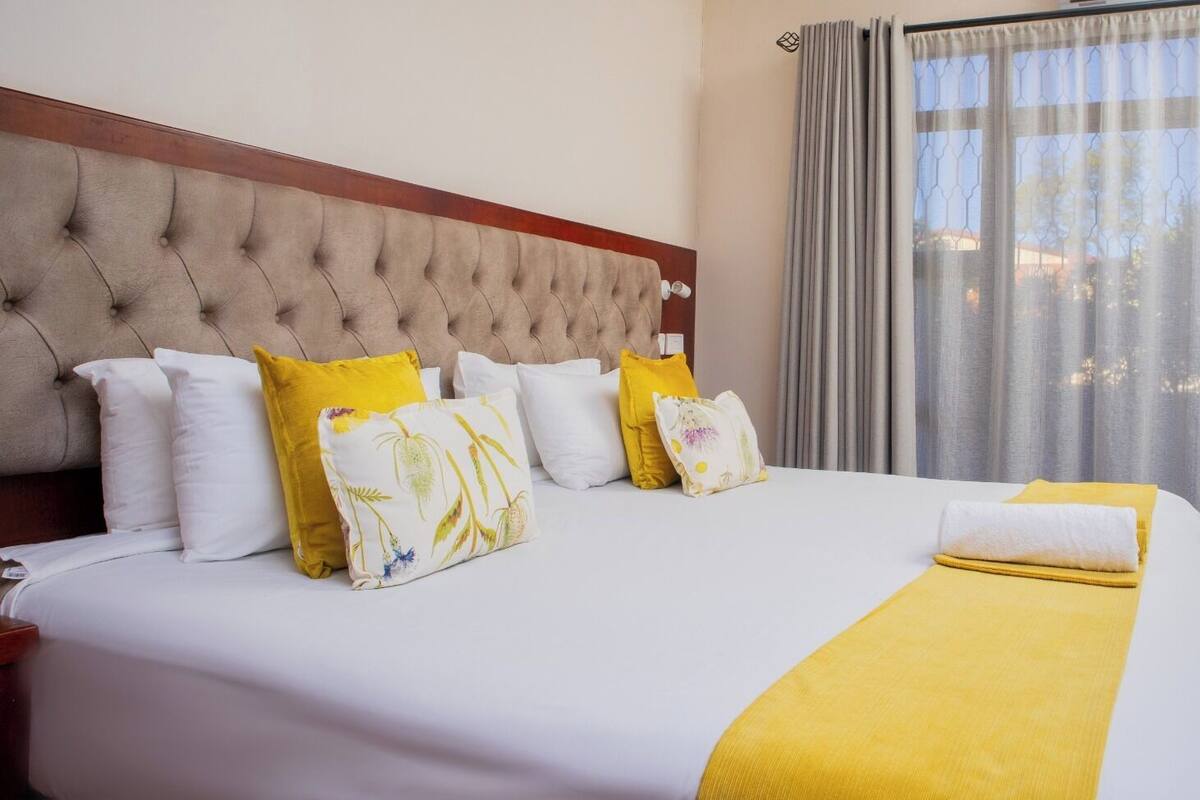 A hotel room with a large bed, multiple pillows, a headboard, and a window with curtains.