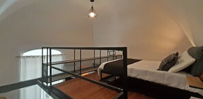A bedroom with a bunk bed, a glass railing, a hanging light fixture, and a white curtain.